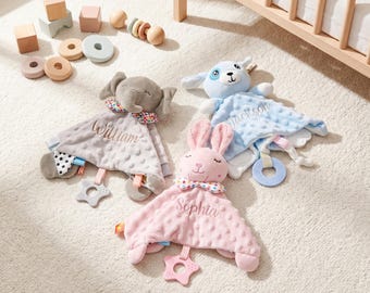 May include: Three plush security blankets featuring an elephant, a rabbit, and a dog. The gray elephant is embroidered with William, the pink rabbit with Sophia, and the blue dog with Jackson. Each blanket has a textured fabric and a star-shaped teether.