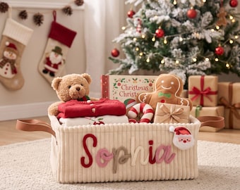 May include: A cream-colored corduroy storage basket with brown leather handles, featuring the name Sophia in multi-colored fabric letters and a Santa Claus patch. The basket is filled with a teddy bear, a book, and a gingerbread man toy.