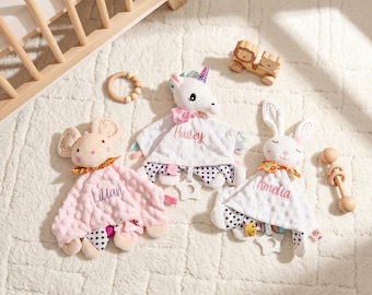 Könnte beinhalten: Drei Plüsch-Schmusetücher in Form einer Maus, eines Einhorns und eines Hasen mit den eingestickten Namen Lilian, Hailey und Amelia. Jedes Tuch hat einen strukturierten Stoffkörper, eine gemusterte Unterseite und einen sternförmigen Beißring.