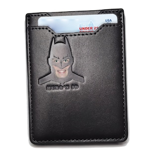 May include: Black leather wallet with a Batman silhouette and the text "HERO'S ID". The wallet has a slot for a card or ID.