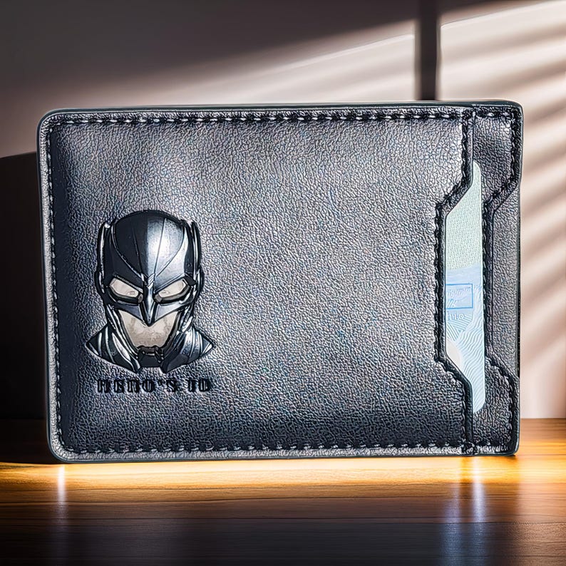 May include: Black leather wallet with a Batman logo and a clear plastic card holder. The wallet has a stitched edge and the text "HERO'S ID" is printed on the front.