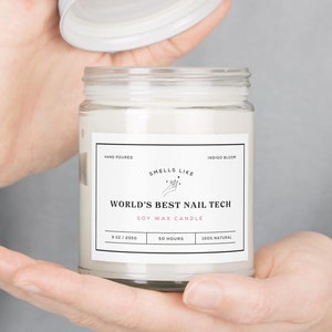 May include: A white soy wax candle in a glass jar with a white lid. The label reads "HAND POURED", "SMELLS LIKE", "WORLD'S BEST NAIL TECH", "SOY WAX CANDLE", "8 OZ / 255G", "50 HOURS", "100% NATURAL", and "INDIGO BLOOM".