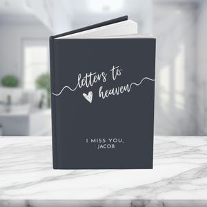 May include: A dark gray journal with the text "letters to heaven" and a heart symbol. The text "I miss you, Jacob" is printed below the title.