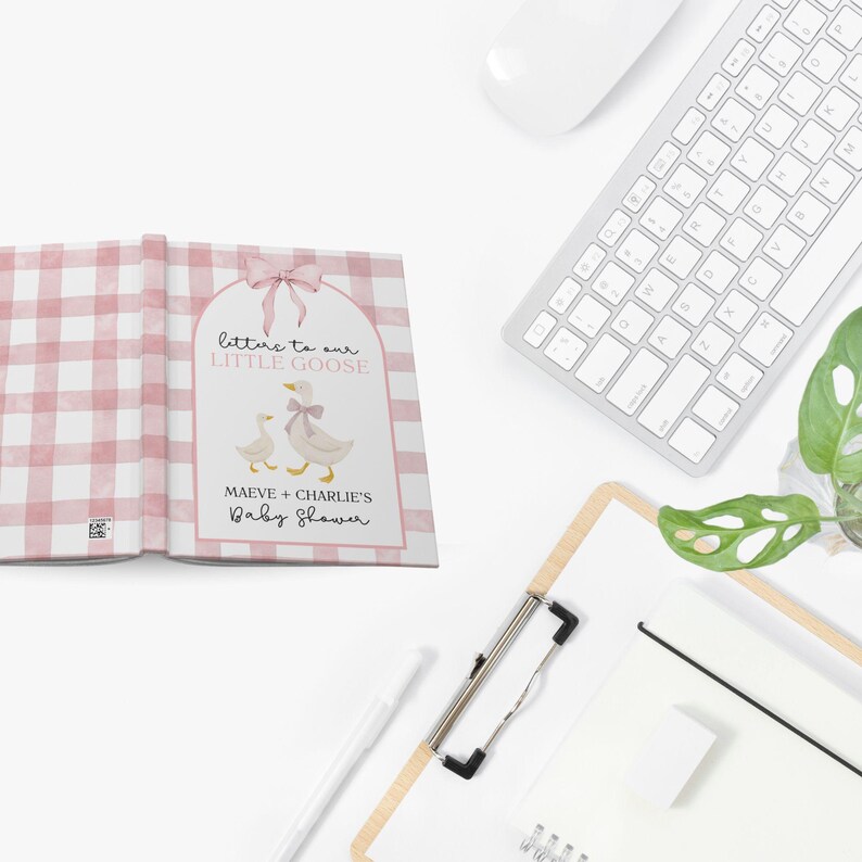 May include: A baby shower guest book with a pink gingham pattern. The cover features a watercolor illustration of two geese and the text "Letters to our Little Goose." The book is open, revealing blank pages.