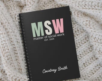 Könnte beinhalten: Schwarzes Spiralnotizbuch mit den Buchstaben "MSW" in Grün und Rosa, darunter "master of social work" und "EST. 2025". Der Name "Courtney Smith" ist unten in Schreibschrift aufgedruckt. Das Notizbuch liegt auf einer cremefarbenen Strickoberfläche.