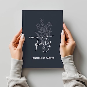 Könnte beinhalten: Ein dunkelblaues Tagebuch mit einem weißen Blumenmuster und dem Text "Kapitel Vierzig" und "Annaliese Carver".