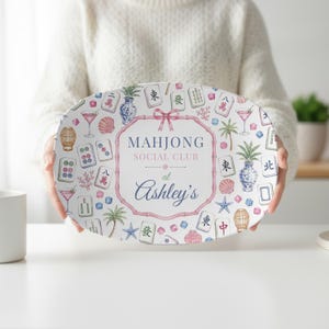 May include: An oval serving platter featuring a central pink bamboo-style frame with the text "MAHJONG SOCIAL CLUB at Ashley's". The background is decorated with colourful illustrations of mahjong tiles, palm trees, cocktails, and seashells.