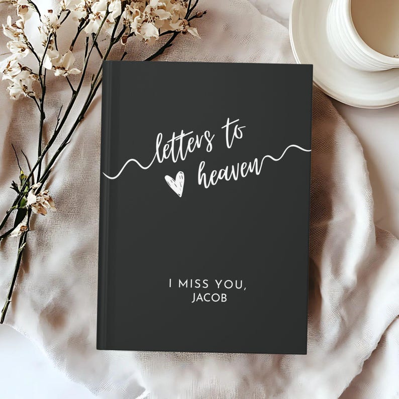 May include: Black journal with white text that reads "letters to heaven" with a heart symbol and the words "I miss you, Jacob".