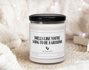 Puede incluir: Una vela blanca en un tarro de cristal con tapa negra. La etiqueta dice "Smells Like You're Going to Be a Grandma" con el texto "Est. June 2025" y huellas de bebé. La vela es de 255 g.
