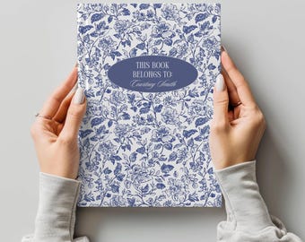 Puede incluir: Un libro blanco con un patrón floral azul y el texto "This book belongs to: Courtney Smith" en un óvalo azul.