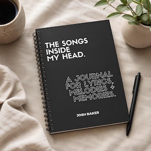 May include: A black spiral-bound journal with white text that reads THE SONGS INSIDE MY HEAD. A JOURNAL FOR LYRICS, MELODIES + MEMORIES. JOSH BAKER. The cover features a matte finish and a clean, modern layout with bold and outlined white typography.