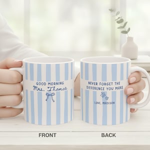 May include: Two white ceramic mugs with vertical light blue stripes. The front mug features the text "GOOD MORNING Mrs. Thomas" with a small blue bow icon. The back mug displays the text "NEVER FORGET THE DIFFERENCE YOU MAKE" and "LOVE, MADISON" with two small blue flower icons.