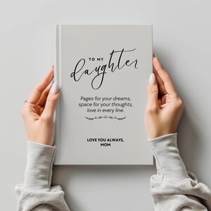 May include: A light gray journal held by two hands. The cover reads "TO MY Daughter" in elegant script, with the text "Pages for your dreams, space for your thoughts, love in every line." Below, it says "LOVE YOU ALWAYS, MOM."