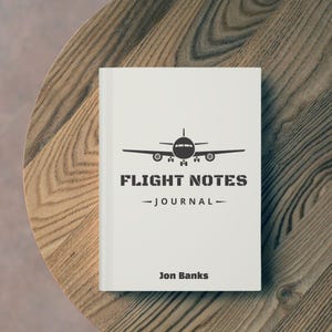 May include: White book with a black airplane silhouette and the text "Flight Notes - Journal - Jon Banks".
