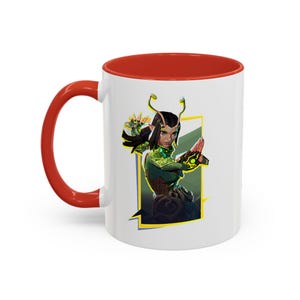 May include: White ceramic coffee mug with a red rim. The mug features a colorful illustration of a female character with green and yellow accents, set against a white and yellow background.