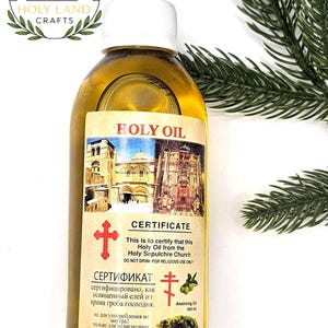 Pode incluir: Uma garrafa transparente de Óleo Sagrado com tampa branca e rótulo com imagens e texto religiosos. O rótulo diz "Holy Oil" e inclui um certificado. A garrafa contém 300 ml de óleo de unção.