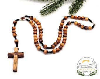 Può includere: Un rosario in legno con perline a forma di oliva e un ciondolo a forma di croce. La croce è incisa con la parola "Gerusalemme". Le perline sono infilate su un cordoncino nero. Un oggetto religioso.