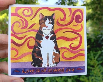 May include: A square card featuring a seated cat illustration with a heart pendant. The cat has brown, black, and white fur, set against a yellow and red swirl background. The text "Love is all around you" is at the bottom.
