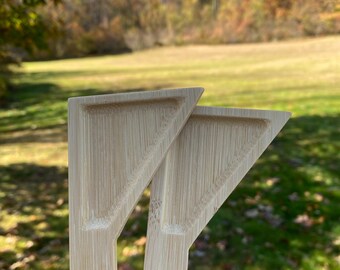 May include: Two wooden triangular serving utensils made of bamboo. The utensils are light brown in color and have a smooth, polished finish.