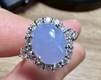 May include: A silver ring featuring a large, oval, pale blue gemstone surrounded by a halo of small, clear gemstones. The ring's setting is silver-colored, and the gemstones are round-cut.
