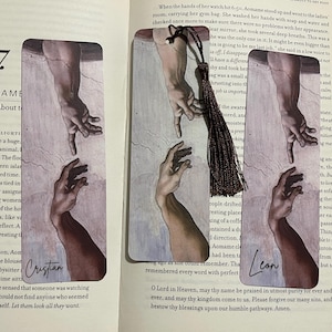 May include: Set of three rectangular bookmarks featuring a detail from Michelangelo's The Creation of Adam. Each bookmark shows two hands reaching out. One bookmark has the name "Cristian" and another has the name "Leon".