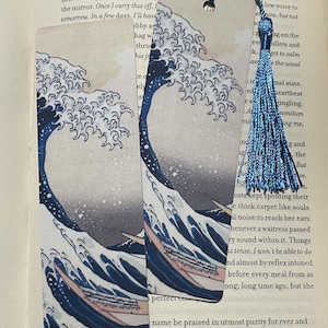 May include: Two rectangular bookmarks featuring a print of Hokusai's "The Great Wave off Kanagawa." The bookmarks have a blue tassel attached. The artwork depicts a large ocean wave with a boat and a mountain in the background.