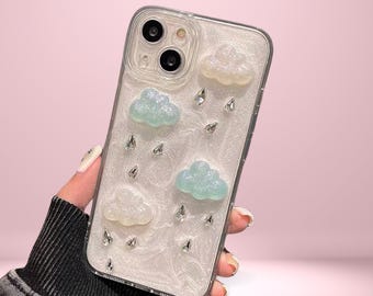 May include: Clear phone case with a white pearlescent background, adorned with light blue and white cloud-shaped embellishments and sparkling teardrop-shaped rhinestones. The text "Cover Boutiquee" is at the top.