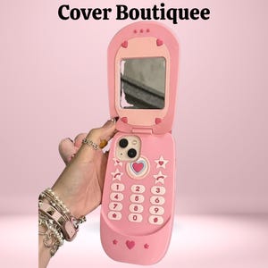 Puede incluir: Funda rosa para teléfono plegable con espejo, detalles de corazón y estrella. La funda tiene un diseño de teclado con números y un botón en forma de corazón. El texto "Cover Boutiquee" está en la parte superior.