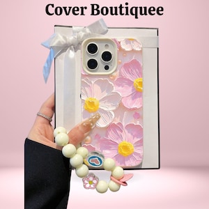 May include: A pink phone case with a floral design featuring white and pink flowers with yellow centres. The case is held in a white gift box with a white bow. The text "Cover Boutiquee" is at the top.