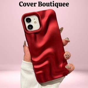 Puede incluir: Funda de teléfono roja con textura ondulada y recorte para la cámara. La funda se muestra sobre un fondo rosa. El texto "Cover Boutiquee" está en la parte superior de la imagen.