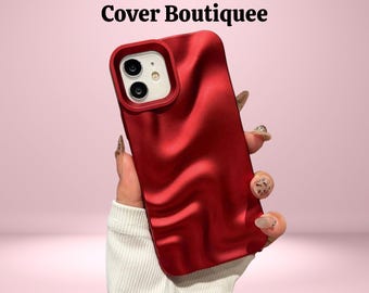 May include: A red phone case with a wavy texture, featuring a camera cutout. The case is held against a pink background. The text "Cover Boutiquee" is at the top of the image.