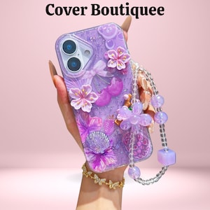 May include: A purple phone case with floral and glitter embellishments. The case features 3D flowers, a seashell, and a beaded strap. The text "Cover Boutiquee" is at the top.