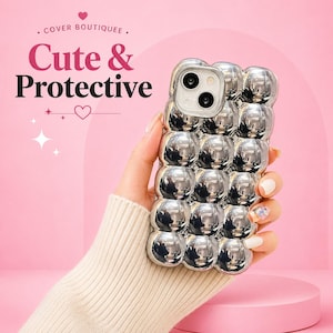May include: A silver phone case with a bubbly, textured design. The case has a camera cutout and the words "Cute & Protective" in pink and black. The background is a soft pink.
