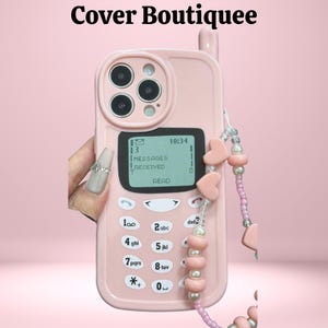 Puede incluir: Una funda de teléfono rosa con un diseño retro, con una pantalla que muestra "MENSAJES RECIBIDOS" y un teclado. La funda tiene una correa de cuentas con dijes en forma de corazón. El texto "Cover Boutiquee" está en la parte superior.