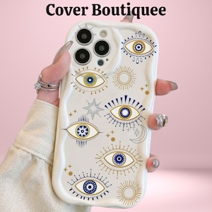 May include: White phone case with a wavy edge, featuring a repeating pattern of stylized blue and gold eyes, stars, and suns. The text "Cover Boutiquee" is at the top. The case is held by a person.