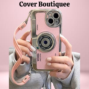 May include: Pink phone case with a camera lens design and a matching pink strap. The case has a silver frame and the text "W088A" is visible. The words "Cover Boutiquee" are at the top.