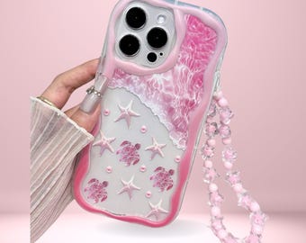 May include: A pink and clear phone case with a beach-themed design. The case features a wave pattern, starfish, and sea turtles. The case has a pink beaded strap and the text "Cover Boutiquee" at the top.