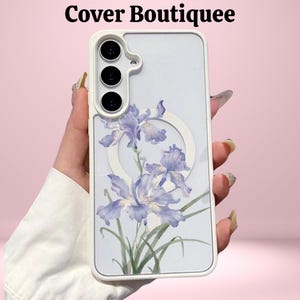 May include: A white phone case with a floral design featuring light purple irises and green leaves. The case has a white border and a circular design element. The text "Cover Boutiquee" is at the top.