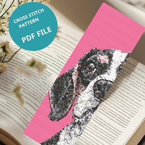 May include: A pink cross-stitch bookmark featuring a black, white, and gray dog design. The bookmark is set against an open book. Text on the bookmark reads "CROSS STITCH PATTERN PDF FILE".