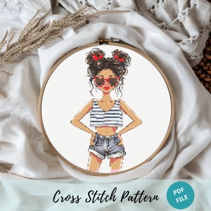 May include: Cross stitch pattern featuring a cartoon girl with brown hair in two buns, wearing a striped tank top, denim shorts, and red heart-shaped sunglasses. The pattern is in a white embroidery hoop.