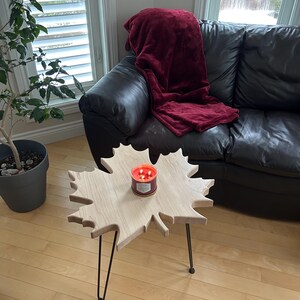 Peut inclure: Une table basse en bois en forme de feuille d'érable avec des pieds en épingle à cheveux noirs. Une bougie est posée sur le plateau de la table.