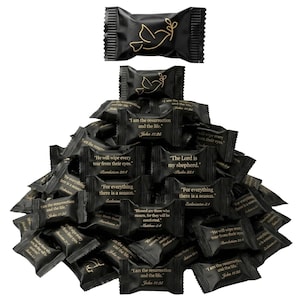 May include: A large pile of individually wrapped black candies with gold text and graphics. Each wrapper features a gold dove icon or a Bible verse, including phrases like I am the resurrection and the life, John 11:25, and The Lord is my shepherd.