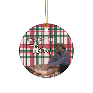 May include: Round ceramic Christmas ornament with a plaid pattern in red, green, and white. The ornament features the text "Hyper on Two." and an image of a person in a blue uniform.