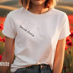 Op de afbeelding: Wit T-shirt met een zwarte omtrek van Saint Croix en de naam in script. Het shirt heeft korte mouwen en is gemaakt van een zacht materiaal. Het woord "White" staat linksonder op het shirt.