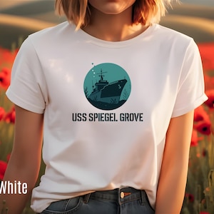 Puede incluir: Camiseta blanca con un gráfico verde azulado de un barco dentro de un círculo verde azulado, con el texto "USS Spiegel Grove" debajo. La camiseta está hecha de un material suave y cómodo.
