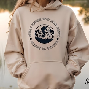 Op de afbeelding: Zandkleurige hoodie met een cirkelvormige afbeelding van een mountainbiker en de tekst "Great Divide Mtn Bike Route Canada to Mexico". De hoodie heeft een voorzak en een capuchon met trekkoord. Het woord "Sand" staat rechtsonder.
