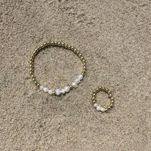 May include: A circular bracelet and a matching ring, both constructed from small, reflective gold-toned metallic beads interspersed with a segment of irregular, white freshwater pearls arranged in a continuous, circular pattern.