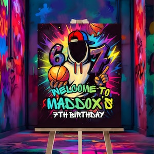 May include: A colorful birthday sign on an easel. The sign features a basketball-themed design with the number 6 and 7, a basketball, and the words "WELCOME TO MADDOX'S 7TH BIRTHDAY". The background is black with neon accents.