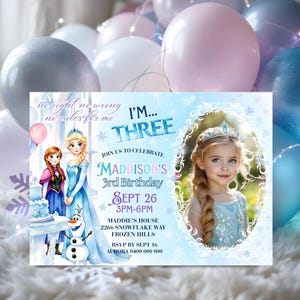 May include: A personalised invitation for a child's third birthday party. The invitation features a photo of a young girl in a blue dress and a princess crown. The invitation has a blue and white snowflake theme with the text "I'm Three".