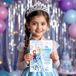 May include: A young girl wearing a silver tiara and a light blue dress holds a birthday invitation featuring Elsa and Anna from Frozen. The invitation reads "I'm Three" and includes party details.